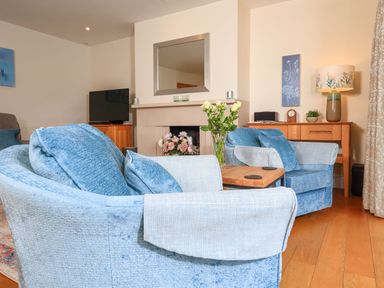 A living room with blue armchairs a wooden table a fireplace with flowers a wooden sideboard and a lamp at 15 Dart Marina in Dartmouth