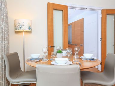 A dining table set with bowls, plates, glasses, and cutlery with chairs around it and a floor lamp beside curtains at 15 Dart Marina Dartmouth