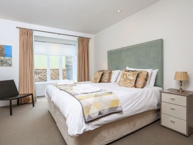 A bedroom with a large bed with pillows and folded towels a bedside table with a lamp a chair and windows with curtains at 15 Dart Marina in Dartmouth