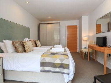 A bedroom with a large bed linens and pillows a wardrobe wooden door desk chair and television at 15 Dart Marina in Dartmouth