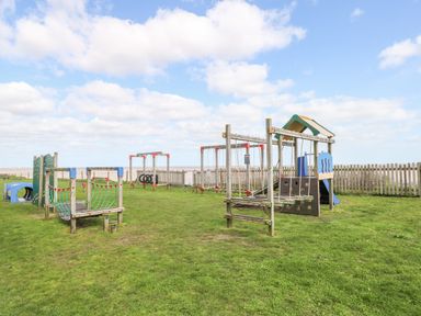 An outdoor playground with climbing frames swings and a slide on grass near a wooden fence at Bungalow 14 in Corton