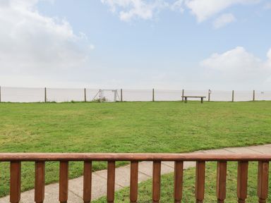 A grassy area with a wooden fence and a bench near a wire fence and gate at Bungalow 14 in Corton