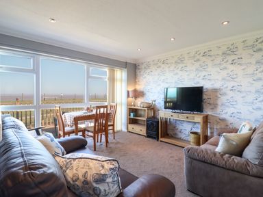 A living room with two sofas a dining table and chairs a television on a wooden stand and large windows overlooking a grassy area at Bungalow 14 in Corton