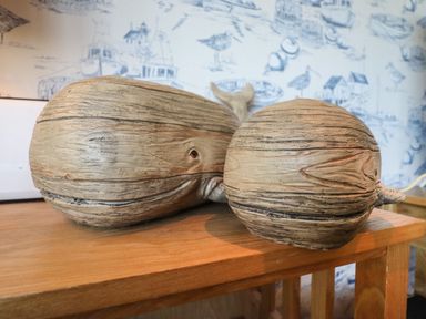 Two wooden whale sculptures on a wooden table with blue and white wallpaper in the background at Bungalow 14 in Corton