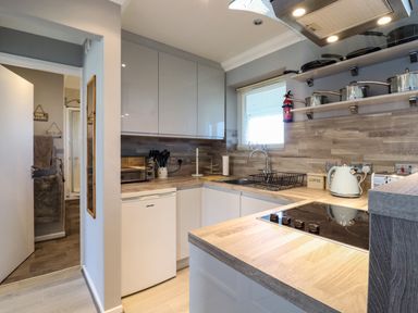 A kitchen with white cabinets a cooktop pots on shelves and a sink at Bungalow 14 in Corton