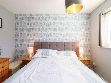 A bedroom with a bed with white and light blue bedding two bedside tables with lamps wallpaper with blue and white houses at Bungalow 14 in Corton