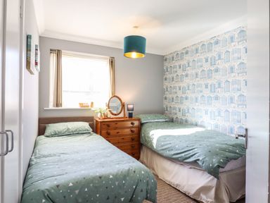 A bedroom with two single beds a wooden chest of drawers a window and patterned wallpaper at Bungalow 14 in Corton