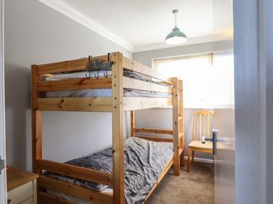 A small bedroom with wooden bunk beds a chair near the window and a bedside table at Bungalow 14 in Corton