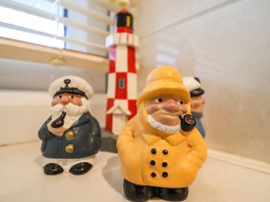 Three ceramic sailor figurines and a red and white lighthouse model on a surface near a window at Bungalow 14 in Corton