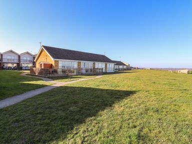A row of single-story houses with wooden fences and large windows on a grassy area at Bungalow 14 in Corton