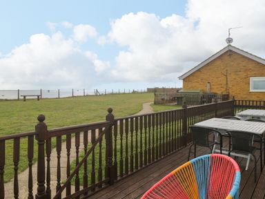 A deck with tables and chairs overlooking a grassy yard and a brick house at Bungalow 14 in Corton