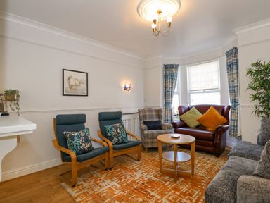 A living room with chairs a small table and window curtains at Apple Tree House in Hunstanton