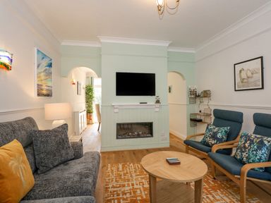 A living room with sofa and armchairs facing a fireplace and wall mounted TV at Apple Tree House in Hunstanton