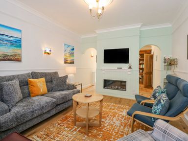 A living room with a gray sofa yellow pillow blue armchairs wooden coffee table and wall-mounted tv at Apple Tree House in Hunstanton