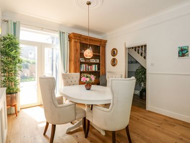 A dining room with a white round table surrounded by four beige chairs and a wooden bookcase at Apple Tree House in Hunstanton