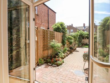 A garden with brick paving and plants along a wooden fence at Apple Tree House in Hunstanton