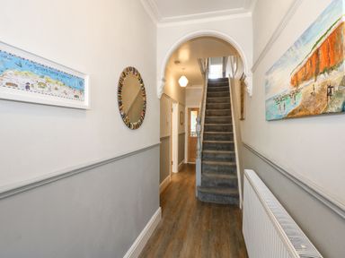A hallway with wooden floor stairs and paintings on the walls at Apple Tree House in Hunstanton