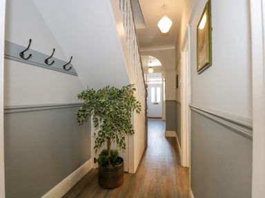 A hallway with wooden floor a potted plant under stairs wall hooks and a door at Apple Tree House in Hunstanton