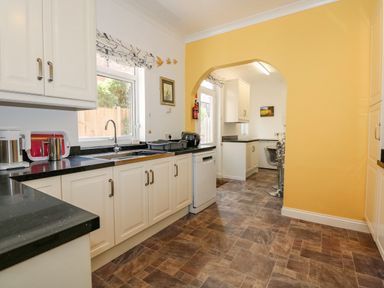 A kitchen with white cabinets black countertops a sink a dishwasher and a yellow wall at Apple Tree House in Hunstanton