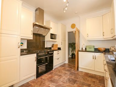 A kitchen with white cabinets a black oven a microwave and a green bread bin at Apple Tree House in Hunstanton