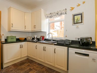 A kitchen with cream cabinets a black countertop a sink under a window and various appliances at Apple Tree House in Hunstanton