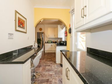 A kitchen with black countertops white cabinets bar stools and an archway at Apple Tree House in Hunstanton