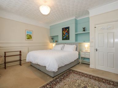 A bedroom with a double bed bedside tables lamps and paintings at Apple Tree House in Hunstanton