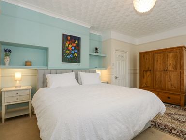 A bedroom with a large bed two nightstands with lamps a wooden wardrobe and a floral painting on the wall at Apple Tree House in Hunstanton