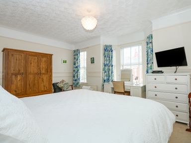 A bedroom with a wooden wardrobe a white dresser with a TV and a vanity table with a chair at Apple Tree House in Hunstanton