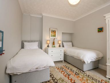 A bedroom with two single beds a white chest of drawers and a patterned rug at Apple Tree House in Hunstanton