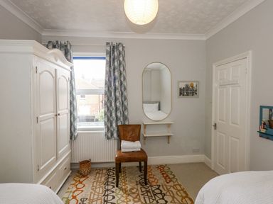 A bedroom with a white wardrobe a window with curtains a brown chair with towels a wall mirror and a door at Apple Tree House in Hunstanton
