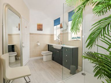 A bathroom with a toilet, sink with cabinet, large mirror, chair, and glass shower at Apple Tree House in Hunstanton