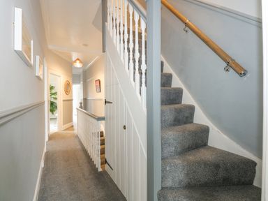 A hallway with carpeted stairs and a railing with doors and framed pictures on the wall at Apple Tree House in Hunstanton
