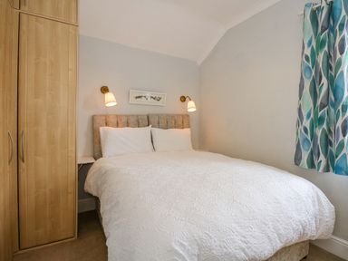 A bedroom with a double bed white bedding bedside tables wall lamps wooden wardrobe and patterned curtains at Apple Tree House in Hunstanton