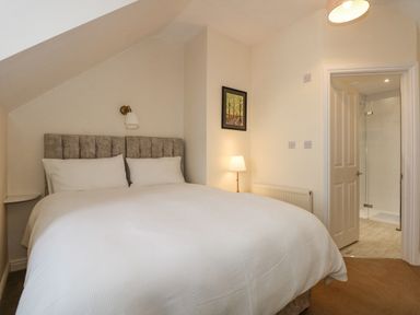 A bedroom with a double bed white bedding a lamp and an open door leading to a bathroom at Apple Tree House in Hunstanton