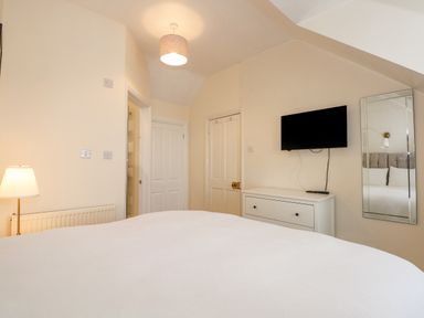 A bedroom with a bed a dresser a wall-mounted television a floor lamp and a wall mirror at Apple Tree House in Hunstanton
