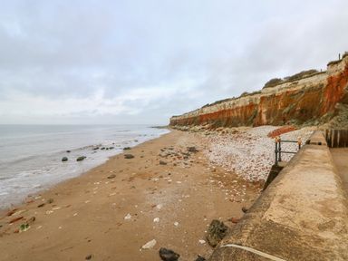 A sandy beach with rocks along the shoreline and cliffs in the background at Apple Tree House in Hunstanton