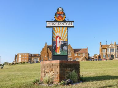 A grass field with a colorful carved sign saying Hunstanton and buildings in the background at Apple Tree House in Hunstanton