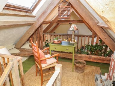 A loft area with a wooden chair by a green table with plants and a lamp at The Byre in Monkleigh near Great Torrington