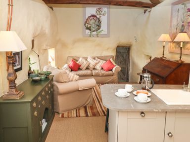 A living room with sofas and a wooden cabinet next to a kitchen island with cups and a coffee press at The Byre in Monkleigh near Great Torrington