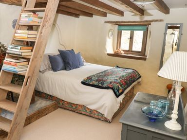 A bedroom with a bed pillows a floral blanket a wooden ladder with books and a window at The Byre in Monkleigh near Great Torrington