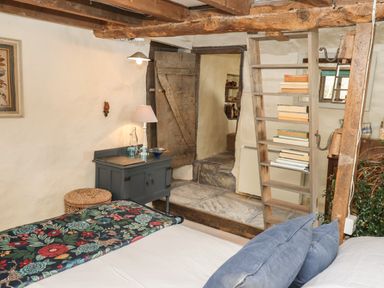 A bedroom with a bed a wooden ladder with books and a rustic wooden door at The Byre in Monkleigh near Great Torrington