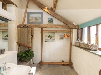 A room with wooden beams a coat rack paintings a plant and a window with baskets at The Byre in Monkleigh near Great Torrington