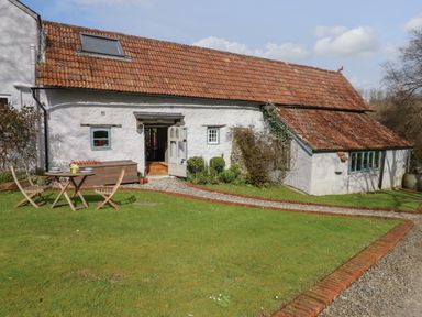 An exterior view of a building with a red tiled roof white walls a wooden table and chairs on the grass at The Byre in Monkleigh near Great Torrington