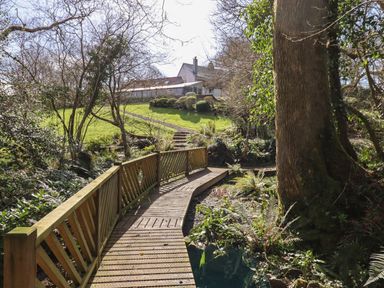 A wooden bridge over a small stream leading to a grassy garden with a house in the background at The Byre Monkleigh near Great Torrington