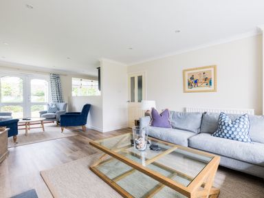 A living room with a glass coffee table a grey sofa with pillows two blue armchairs wooden floors and large windows at Silverdale in Rock