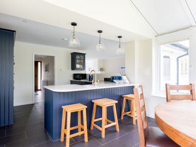 A kitchen with a blue island and wooden stools next to a wooden dining table at Silverdale in Rock