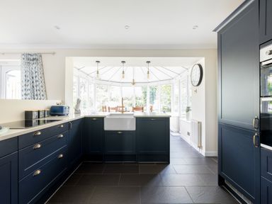 A kitchen with dark blue cabinets and a white sink opening to a dining area with wooden chairs at Silverdale in Rock