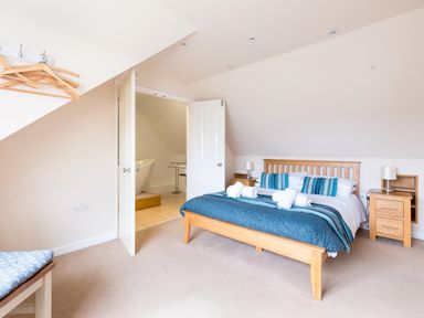 A bedroom with a wooden bed and blue bedding and an open door leading to a bathroom at Silverdale in Rock