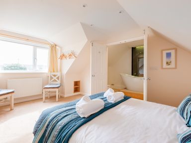 A bedroom with a double bed with rolled towels on it two chairs by a window and an open door leading to a bathroom with a freestanding bathtub at Silverdale in Rock